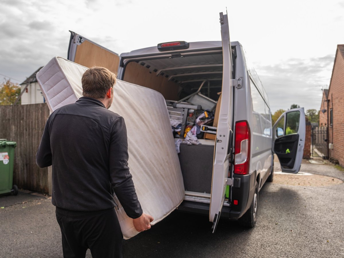 Worker carrying and loading a mattress into a removal van outside a residential building during a cleanout